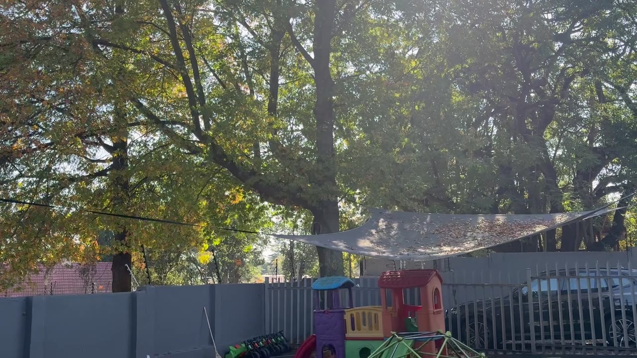 Outdoor play area at Little Lion Pre-School with shade cloth, trees and a toy train